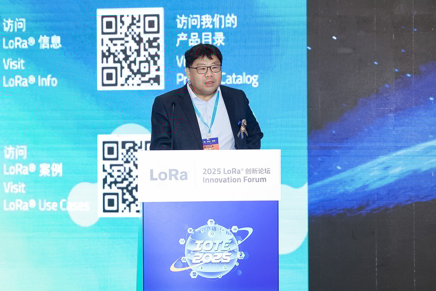 Mike Wong, Vice President of Sales for Asia Pacific at Semtech, delivering the opening speech at the 2025 LoRa Innovation Forum during IOTE Shenzhen, standing at a podium with blue backdrop featuring QR codes and multilingual LoRa information
