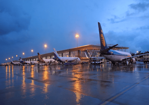 Evening view of Bangalore airport with multiple aircraft parked at gates, including a Jet Airways plane prominently in the foreground. The wet tarmac reflects terminal lights against a twilight blue sky, showcasing the modern airport infrastructure where Enthu Technology's smart water management solutions helped achieve 10% resource savings through real-time monitoring and leak detection systems.