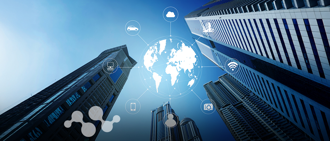 Looking upward at modern skyscrapers converging around a digital globe in the center. The globe is connected to various IoT icons including cloud computing, smart vehicles, WiFi connectivity, mobile devices, security cameras, and computer systems. The blue-tinted image illustrates how smart buildings integrate with digital networks to create an interconnected urban ecosystem, perfectly representing the future of connected spaces transforming our cities.